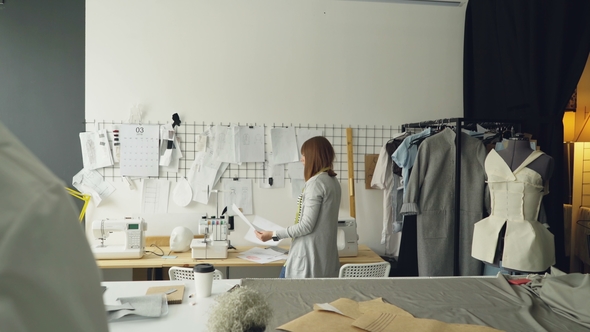 Female Fashion Designer Choosing and Hanging Clothing Sketches on Wall for Her Newest Collection alt