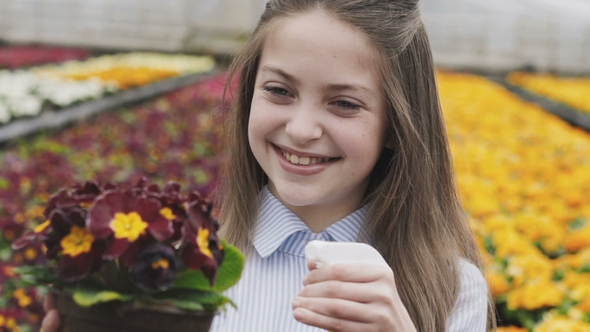 Happy Pretty Girl Spraying Flowerpots in Greenhouse. Slowly alt