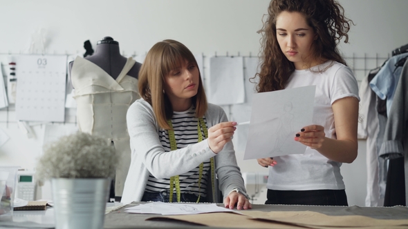 Young Attractive Women Are Looking at Garment Drawing and Discussing It While Working in Modern alt