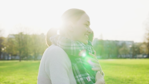 Happy Mother Hugs and Gently Strokes Her Little Child at Sunset in Park