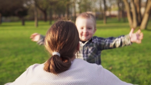 Happy Little Boy Runs into Mother's Open Arms and Hugs Her in Spring Park