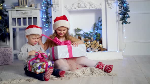 Happy little kids opening presents on Xmas eve. Children under Christmas tree with gift boxes.