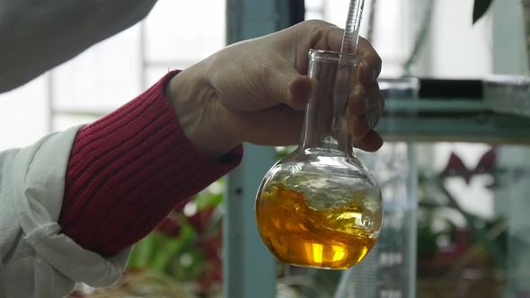 Man`s Hand Spins a Glass Flask with Yellow Liquid and a Tube in a Biotech Lab