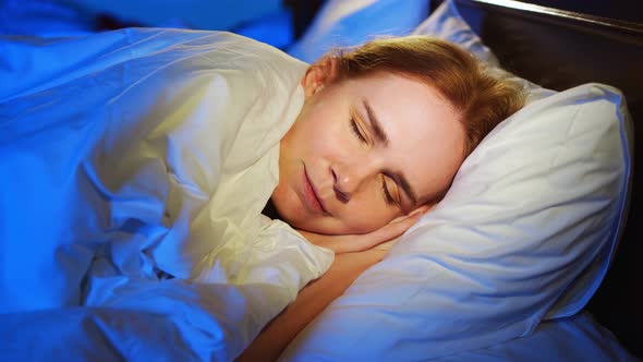 a Woman with Red Hair Sleeps on Her Side in Bed and Sees Quiet Dreams Smiles alt