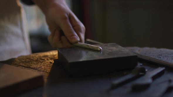 Close up of hands of caucasian female jeweller using hammer, making jewelry alt