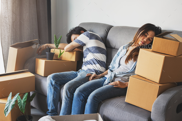 Young tried couple moving in new home, sitting and relaxing on sofa with cardboard boxes Stock Photo by kitzstocker