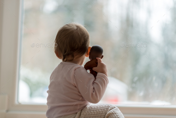 Little baby girl hugging a toy watching the winter snow outdoors Stock Photo by Gajus-Images
