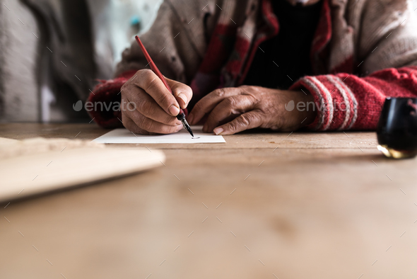 Old man with dirty hands writing a letter using a nib pen and in Stock Photo by Gajus-Images