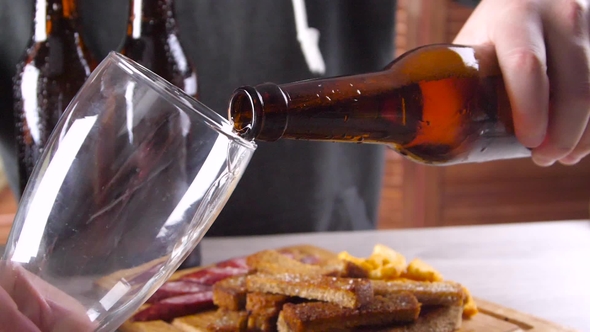 Man at the Table with Beer Snacks Pours Beer Into a Glass alt