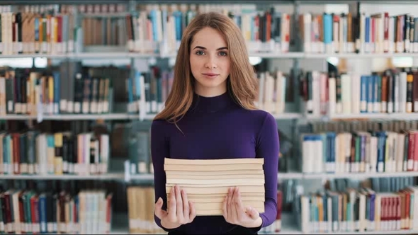 Smiling Female Student Hold Books Standing Before the Shelves in the Library alt