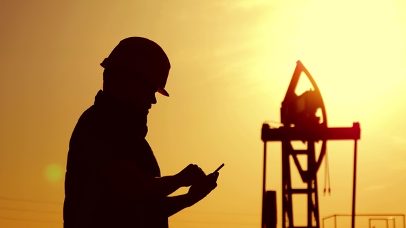Silhouette of Oilfield Worker at Crude Oil Pump in the Oilfield at Golden Sunset. Industry, Oilfield