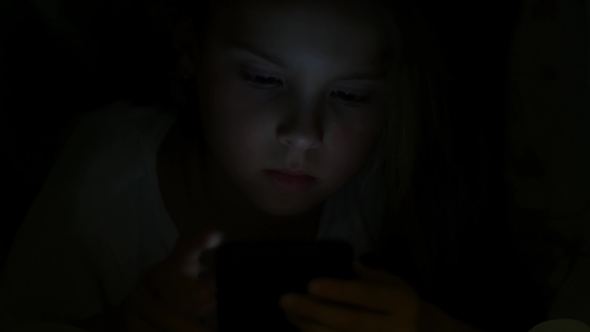 A Girl in Bed Touches the Screen of a Smartphone alt