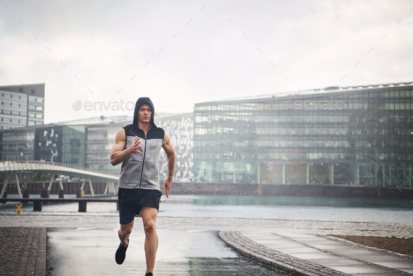 Sportive male running down street in rain - Stock Photo - Images