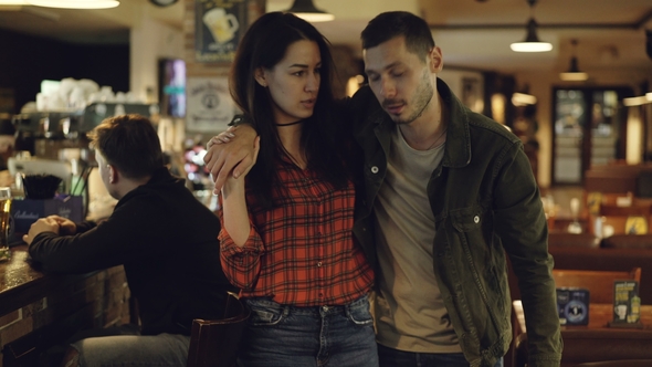 Young Brunette Leading Her Drunk Husband out of Bar, Stock Footage