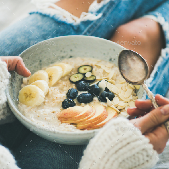 Woman in jeans and sweater eating oatmeal porriage, square crop - Stock Photo - Images