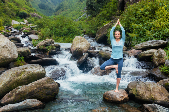 Woman in yoga asana Vrikshasana tree pose at waterfall outdoors Stock Photo  by f9photos