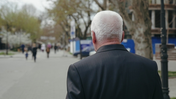 Senior Man in a Business Suit Walks along a Street and Turns around