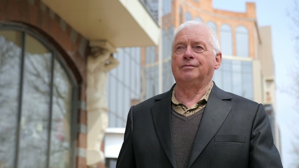 Grey-headed Man in a Jacket Strolls Along a City Street in Spring in