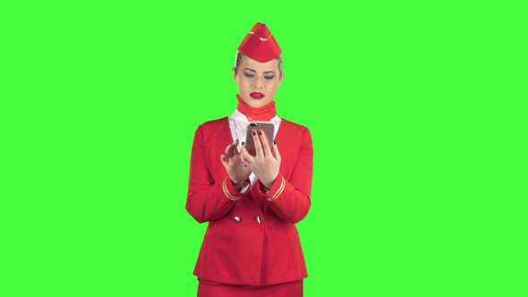 Stewardess in the Red Attire Looks Into the Phone and Is Surprised. Green Screen alt