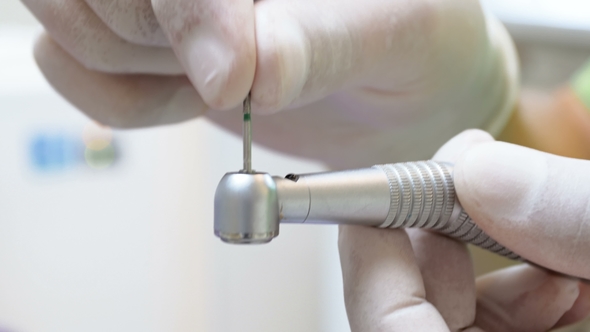 footage of dentist in latex gloves inserting bit in dental drill by