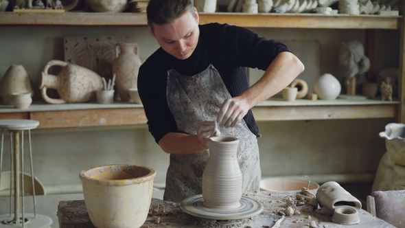 Handsome Young Man Is Molding Ceramic Vase From Clay on Spinning Throwing Wheel While Working alt