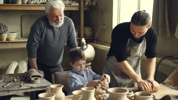 Professional Potter Is Kneading Clay on Worktable in Home Studio While His Son Is Helping Him alt