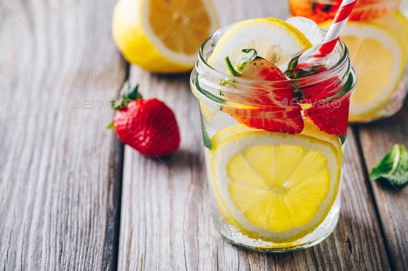Lemon and strawberry lemonade in glass mason jars on a wooden background. Stock Photo by nblxer