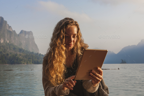 Woman using her tablet by a lake - Stock Photo - Images
