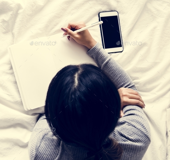 A Woman Writing Down on a Note with Her Phone Nearby - Stock Photo - Images