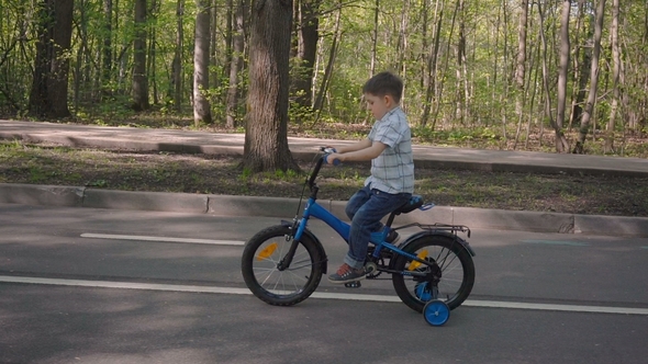 Little Boy Rides Bike Along the City Park. Small Bicyclist Riding Blue Bicycle