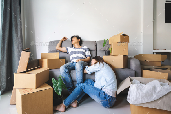 Young tried couple moving in new home, sitting and relaxing on sofa with cardboard boxes Stock Photo by kitzstocker