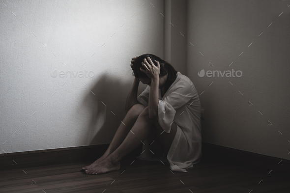 Depressed and stressed woman sitting on the floor alone head in hands in the dark room Stock Photo by kitzstocker