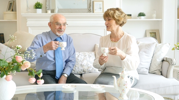 Attractive Senior Couple in Formal Evening Wear, Sitting on the Sofa and Drinking a Tea or Coffee