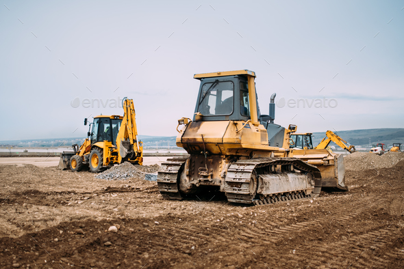 Industrial motor grader and backhoe excavator on highway construction site