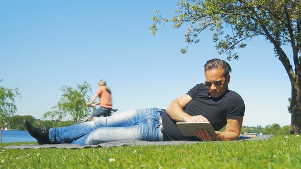 Weekend in the City - a Man Relaxes on the Grass in the Park and Reads a Book