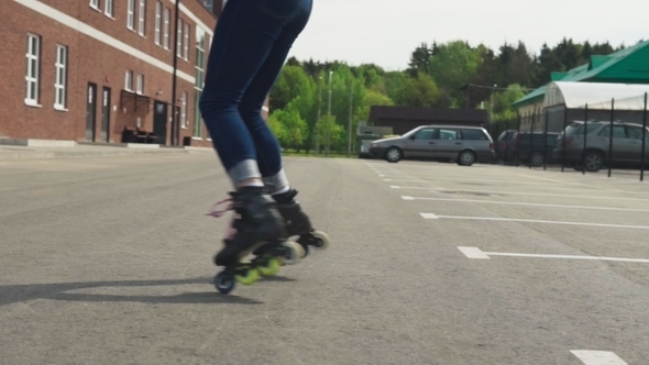 Women's Legs in Roller Skates Whirl Around on Asphalt Road in City alt