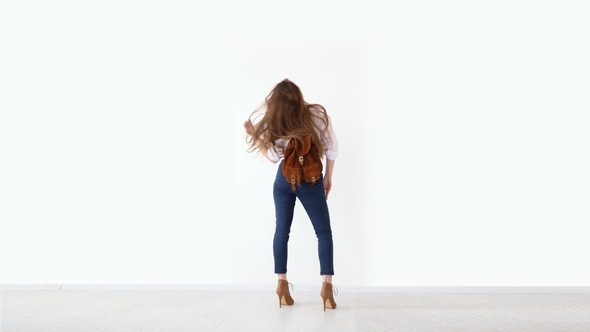 Fashion of Modern Youth. Stylish Girl Posing Against White Wall in Jeans, White Shirt, with Leather
