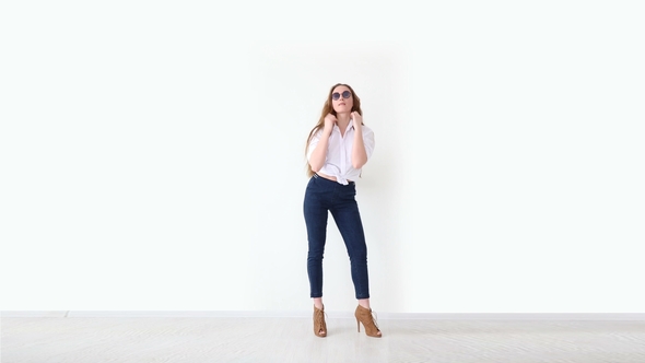 Fashion of Modern Youth. Stylish Girl Posing Against White Wall in Jeans, White Shirt, with Leather