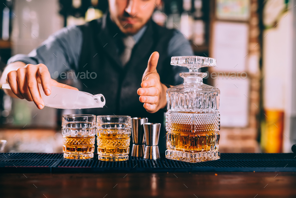 Close up of barman hands adding ice and whiskey to modern urban cocktails. Stock Photo by stockcentral