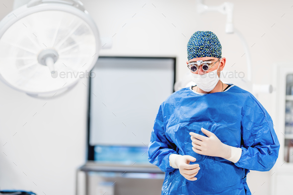 Cosmetic plastic surgeon wearing scrubs, goggles and gloves getting ready for surgery Stock Photo by stockcentral