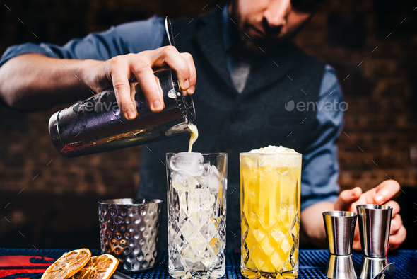 Elegant bartender pouring fresh orange vodka cocktail over ice in crystal glassware Stock Photo by stockcentral
