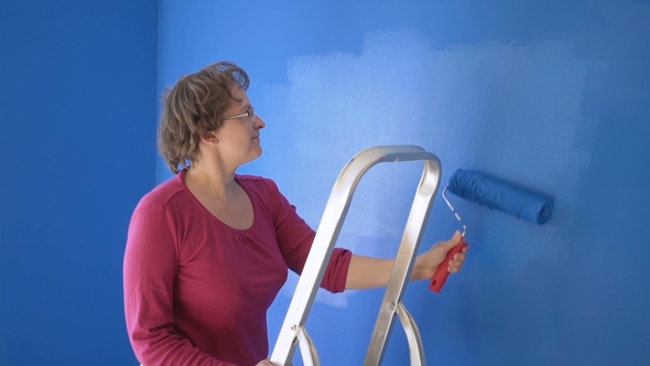 Woman Doing Wall Painting with Blue Paint Standing on the Ladder