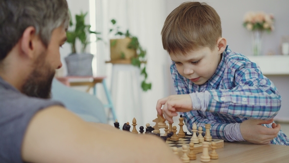 Clever Little Boy Is Learning To Play Chess Moving Chesspieces on Board and Enjoying Playing alt