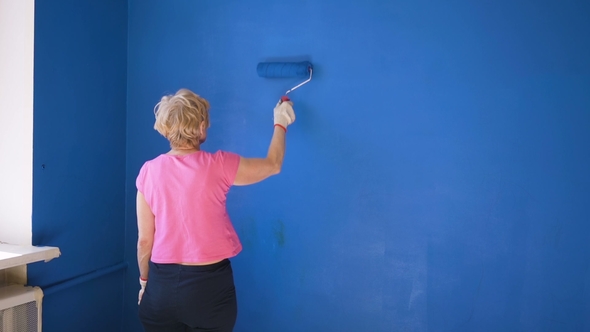Old Woman Painting Interior Wall of House with Blue Paint