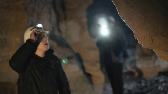 Two Speleologists Exploring the Cave in Darkness. alt