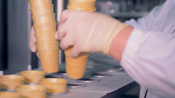 A Pile of Waffle Cups Is Getting Inserted Into the Conveyor Belt By a Factory Worker alt