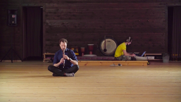 A Man Sitting on the Floor and Playing Flute