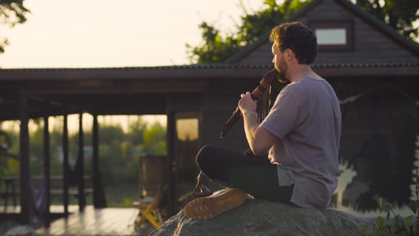 A Man Sitting on a Rock and Playing Ethnic Flute
