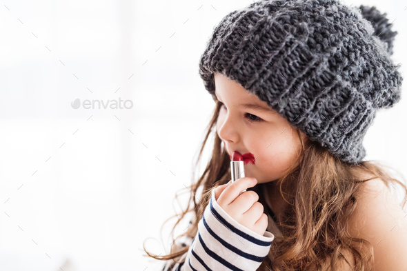 A small happy girl in striped T-shirt at home applying a lipstick. - Stock Photo - Images