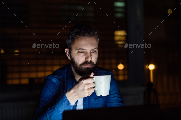 A man working on a laptop at home at night. Stock Photo by halfpoint